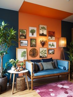 a living room with orange walls and blue couches, potted plants and pictures on the wall