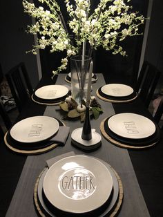 a black table with white plates and flowers in a vase on the centerpieces