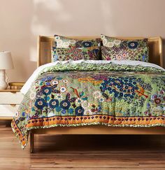 a bed with a colorful comforter on top of it next to a night stand