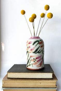 a white vase with yellow flowers sitting on top of two books