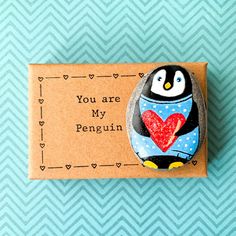 a penguin with a heart painted on it's back sitting next to a card