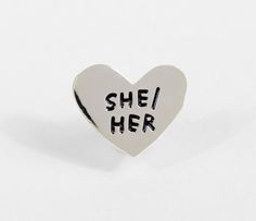 a heart shaped pin with the words she's her written on it in black ink