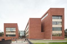 two people are walking in front of a red brick building that has many windows on it