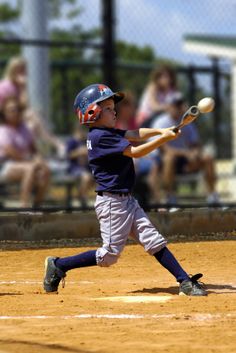 a young boy swinging a baseball bat on top of a field with people in the background