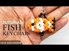 a hand holding a small orange and white beaded keychain