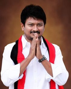 a man in white shirt and red vest standing with his hands folded up to pray