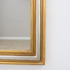 a gold framed mirror hanging on the wall next to a wooden floor and white walls