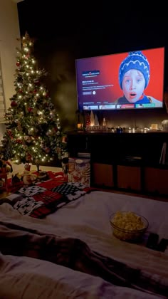 a christmas tree in front of a flat screen tv with a bowl of popcorn on the bed