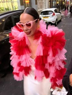 a woman walking down the street wearing pink sunglasses and a red feather bolery jacket