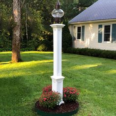 a white clock tower sitting in the middle of a lush green yard