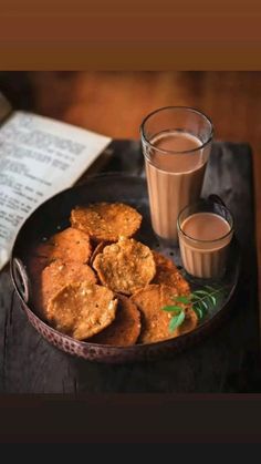 two glasses of milk and some cookies on a tray with an open book in the background