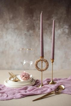 two candles are sitting on a table next to some silverware and a pink blanket