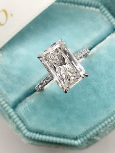 an engagement ring with a princess cut diamond set in a blue velvet box on top of it