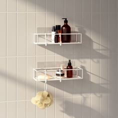 two white shelves with soap, lotion and other items on them against a tiled wall