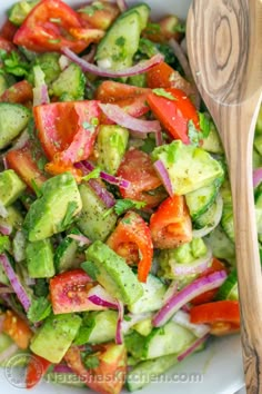 a white bowl filled with cucumber, tomato and onion salad on top of a wooden table