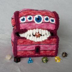 a knitted box with eyes and teeth on the inside, surrounded by dices