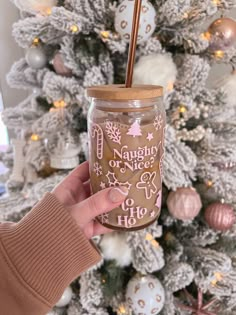 a person holding up a mason jar in front of a christmas tree with ornaments on it