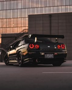 the rear end of a black car parked in front of a tall building with windows