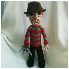 a crocheted doll wearing a hat and holding a pair of scissors in his hand