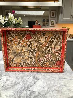 an intricately designed wooden box on a countertop in a kitchen with gray cabinets and white flowers