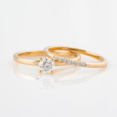 two gold wedding rings with diamonds on top and one diamond in the middle, against a white background