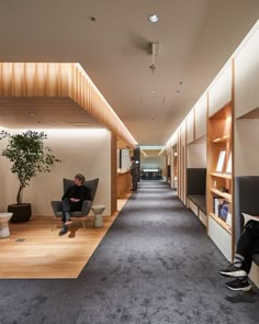 a man sitting in a chair next to a book shelf on the side of a hallway