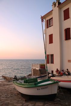 two small boats sitting on the beach next to a white building with red shutters