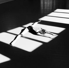 black and white photograph of a woman doing yoga on the floor with long shadows from windows