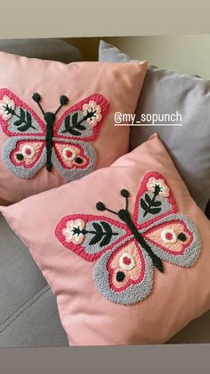 two pink pillows with butterfly appliques on them sitting on a gray couch