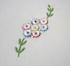 embroidered flowers on white fabric with green stems and blue, yellow, red, and orange pins