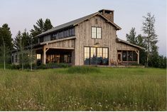 a large wooden house sitting in the middle of a lush green field with tall grass