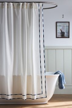 a bath tub sitting next to a shower curtain in a bathroom with white walls and wooden floors