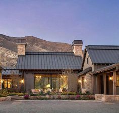 a large house with lots of windows and lights on it's front porch, surrounded by mountains