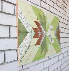 a wooden sign on the side of a white brick wall with green and brown designs