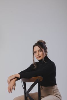 a woman sitting in a chair with her arms crossed and looking at the camera while wearing khaki pants