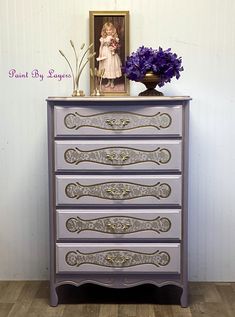 an ornate dresser with purple drawers and gold trimmings on the top, in front of a white wall