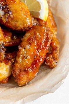 fried chicken wings with lemon wedges and parmesan cheese on the side in a paper bowl