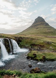 a small waterfall in the middle of a grassy area with a mountain in the background