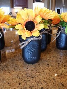 three mason jars with sunflowers tied to them on a countertop in a kitchen