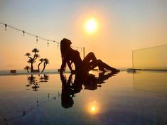 a woman is sitting on the edge of a pool at sunset with her reflection in the water