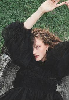 a woman laying on the ground wearing a black dress and holding her hands up in the air