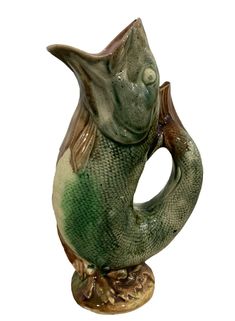 a ceramic fish shaped vase sitting on top of a wooden stand with its mouth open