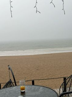 an empty table on the beach with a glass of orange juice in front of it