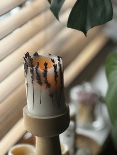 a lit candle sitting on top of a wooden stand next to a potted plant