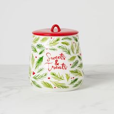 a ceramic cookie jar decorated with pine branches and holly berries, says sweets & treats