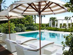 an outdoor pool with lounge chairs and umbrellas next to the swimming pool, surrounded by greenery