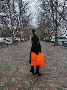 a woman holding an orange shopping bag in the middle of a park