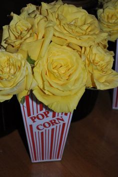 yellow roses are in a popcorn box on the table