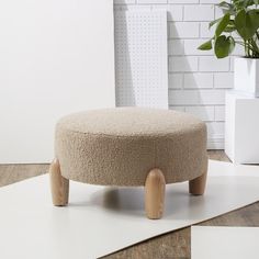 a round ottoman sitting on top of a wooden floor next to a plant in a pot