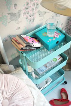 a teal tray with books and magazines on it, sitting next to a bed